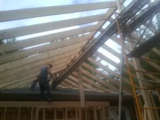 Rafters going up over a new addition with a worker on the wall in Greenville