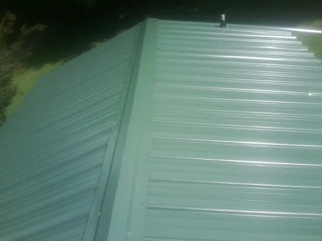 New green metal panels meeting at the ridge of a roof — Flat Roof Repair work by our crew in Greenville